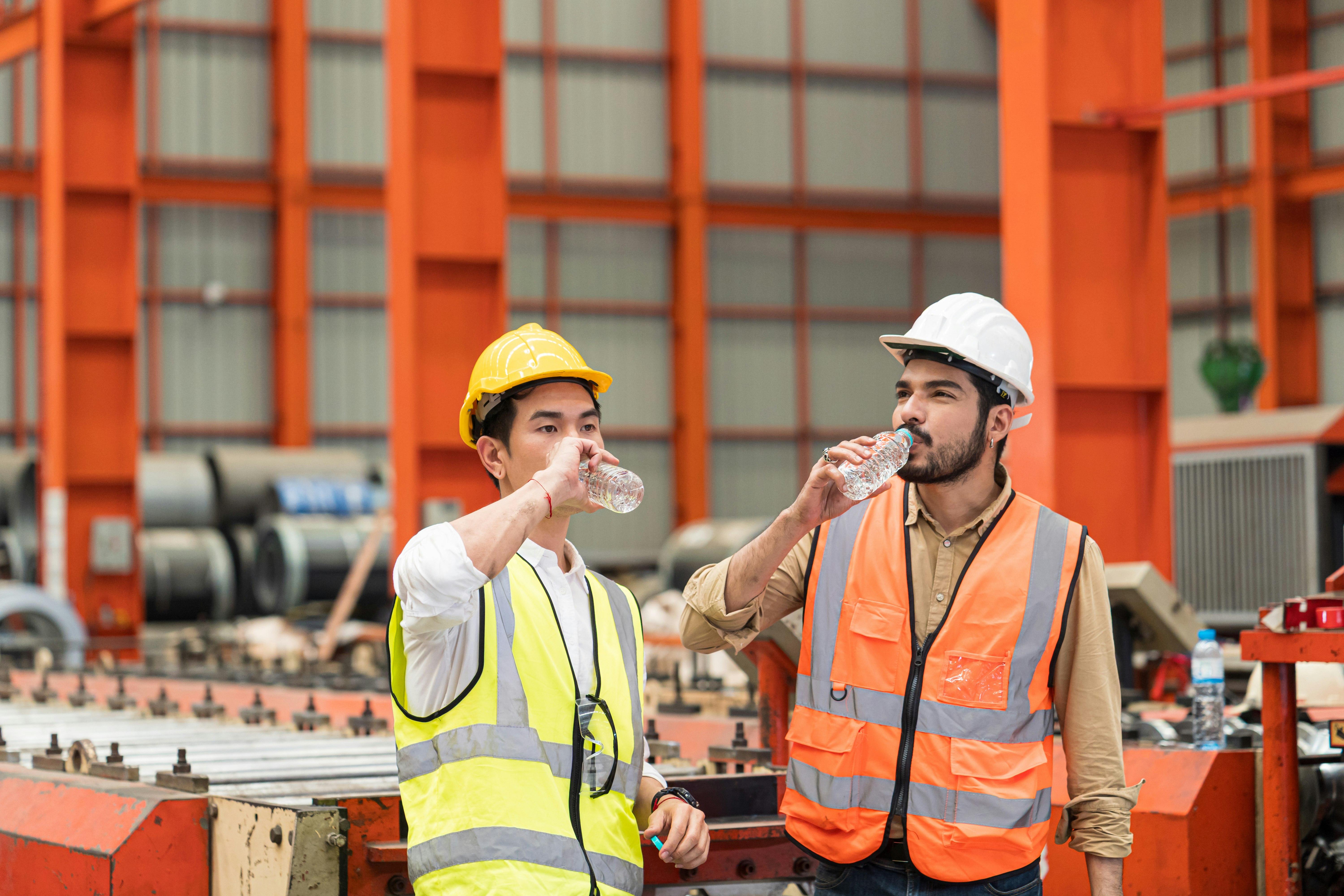 Smiling warehouse workers in safety vests sharing bottles of cold water during a hydration break.